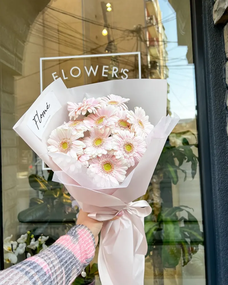 Hand-tied bouquet of pale pink gerberas in blush paper with a Flomé tag