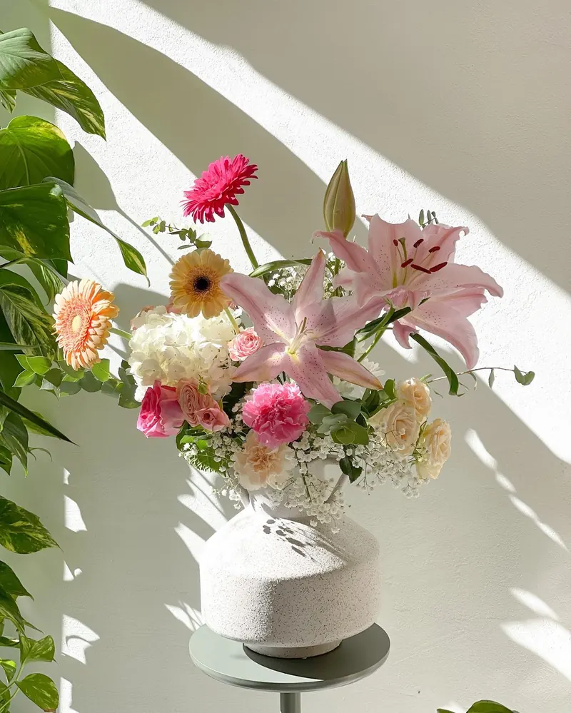 Pink lilies, gerberas and hydrangea arranged in a stone vase in the sun