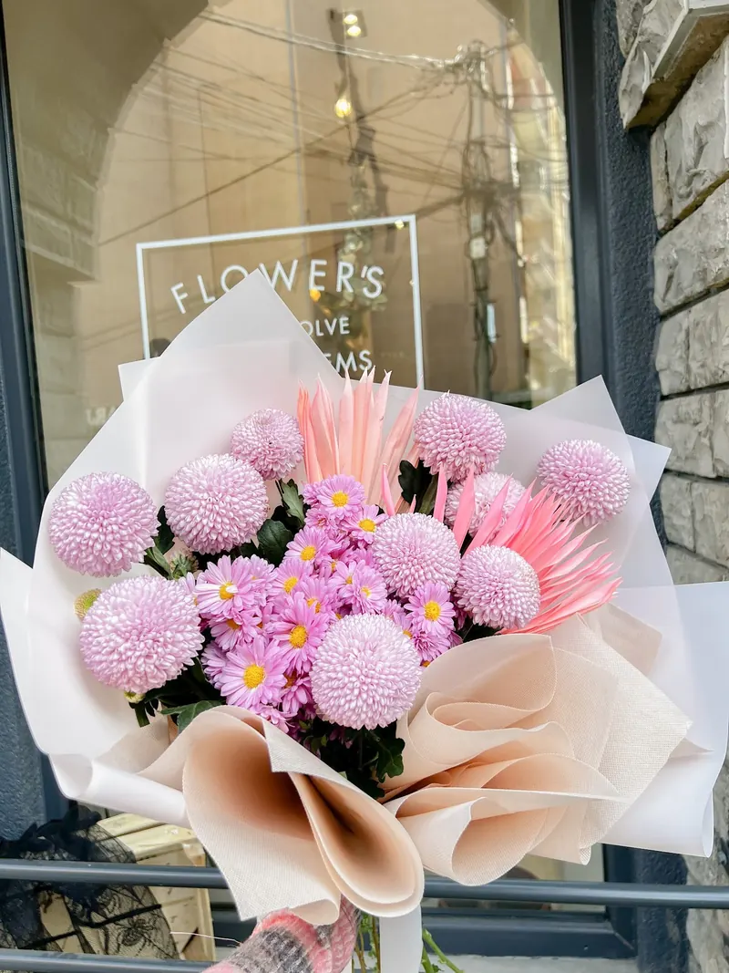 Bouquet of pink pompom chrysanthemums and lilac daisies in peach paper