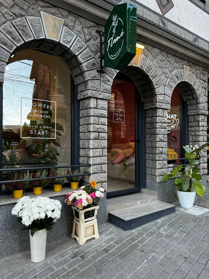 The Flomé storefront: stone arches, a green hanging sign and flowers by the door